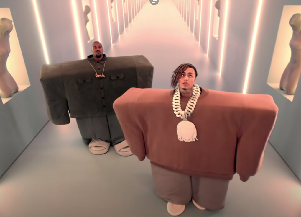 … i'm not sure what this image is? two people in a corridor, looking up, with very wide cuboid bodies, presumably one of them is kanye west